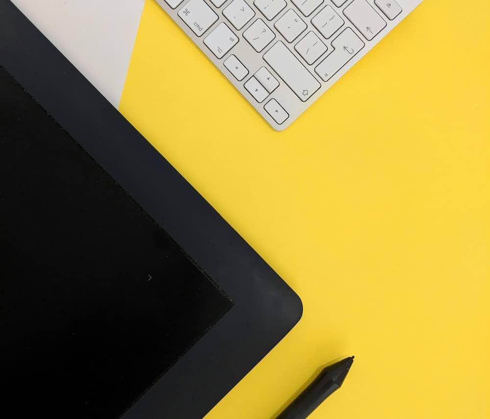 A graphic tablet, stylus, and wireless keyboard are artfully arranged on a bright yellow and white background. This dynamic layout, perfect for any Calgary branding agency, features the tablet in the bottom left corner and the keyboard in the top right. - Clio Websites | Top Canadian Web Design Company