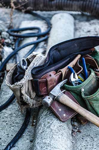 A well-worn tool belt rests on a concrete surface, filled with various tools including a hammer, pliers, and screwdrivers—each as essential as web accessibility in the digital landscape. A black hose and metal pipe are visible in the background. - Clio Websites | Top Canadian Web Design Company