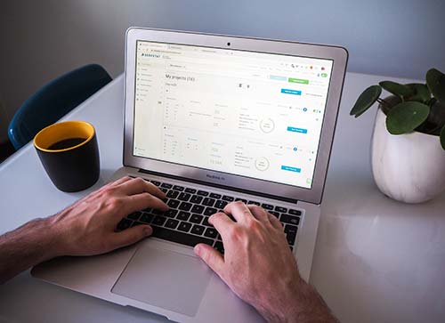 As a person types on a laptop showcasing analytics data, they ponder how a website can help you grow your business. A black and yellow mug sits to the left while a potted plant adds life to the right, both adorning the white desk. - Clio Websites | Top Canadian Web Design Company
