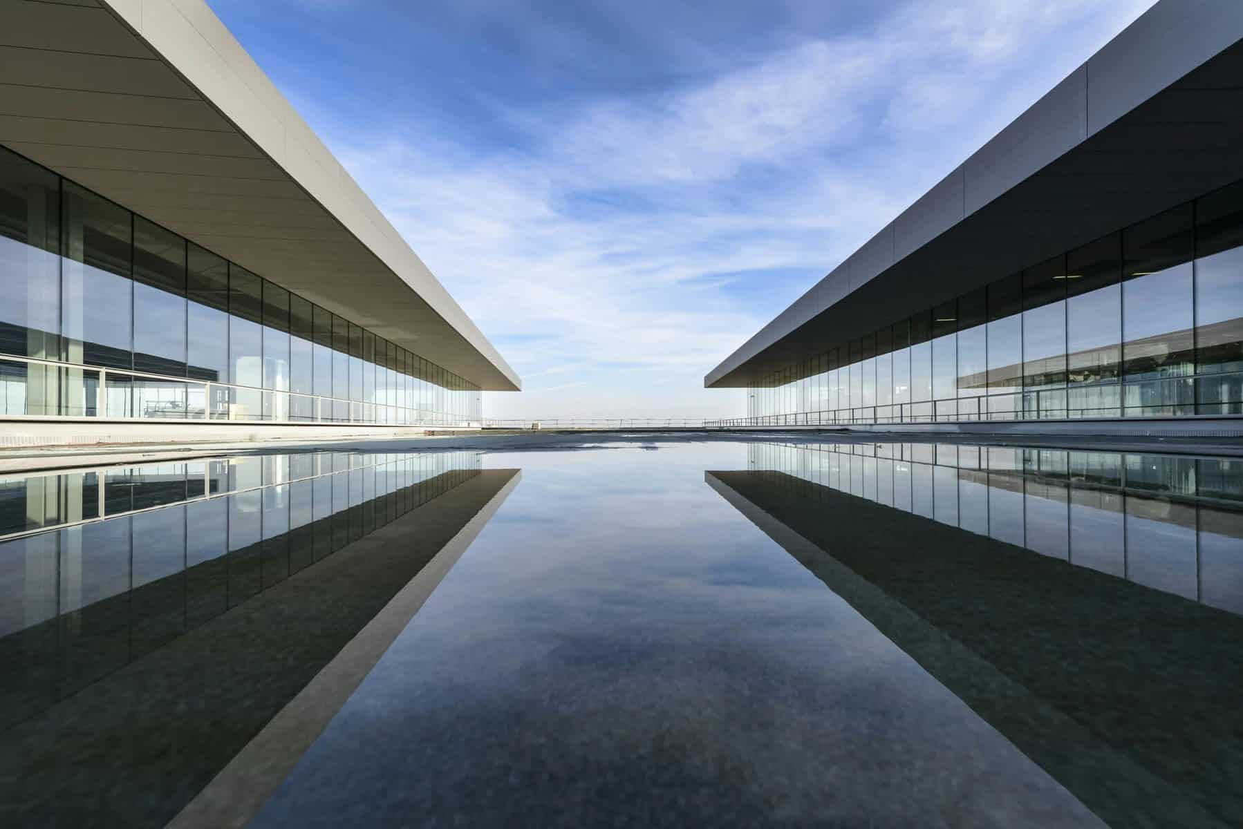 Modern architecture with two glass-walled buildings flanking a reflective water feature, creating a symmetrical perspective that enhances the building's content. The sky above is partly cloudy, complementing the sleek lines of the structures. - Clio Websites | Top Canadian Web Design Company