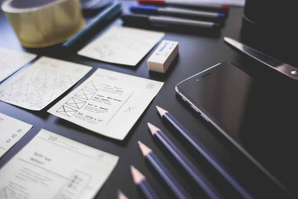 A desk with sticky notes displaying sketches and flow diagrams alongside pencils, pens, a smartphone, scissors, an eraser, and a roll of adhesive tape. These neatly arranged items hint at the creative planning or design process typical of both web designers and web developers. - Clio Websites | Top Canadian Web Design Company