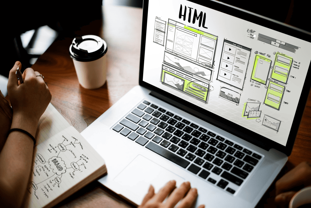 An open laptop displays an HTML design as a person types, while another jots down notes next to a coffee cup on the wooden table—a scene reflecting a business owner delving into eCommerce strategies during their web development session. - Clio Websites | Top Canadian Web Design Company