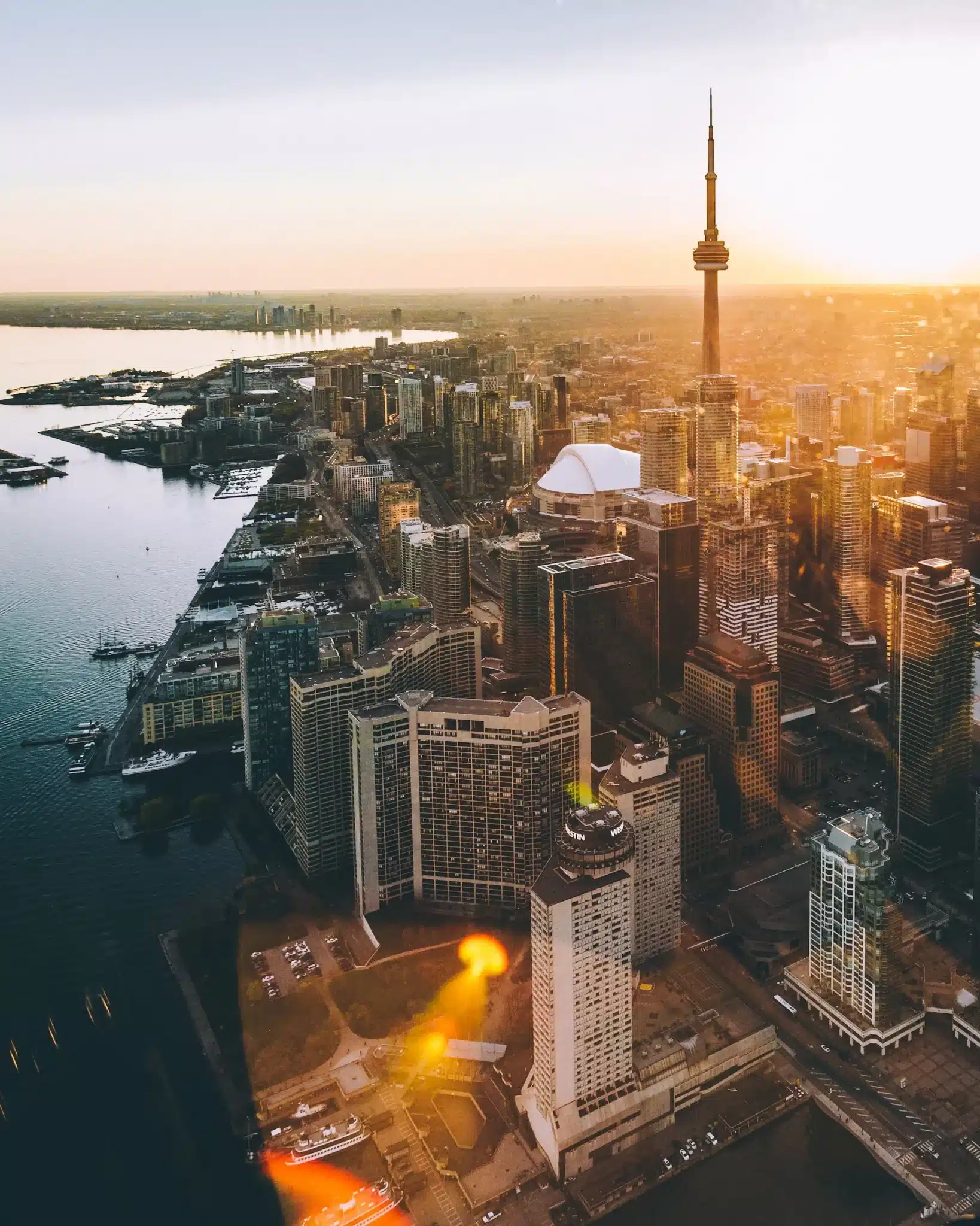 Aerial view of Toronto at sunset, featuring a prominent tower and a skyline of tall buildings. The cityscape, akin to an intricate web design, is bordered by a body of water on the left, with the sunlight casting a warm glow over the scene. - Clio Websites | Top Canadian Web Design Company